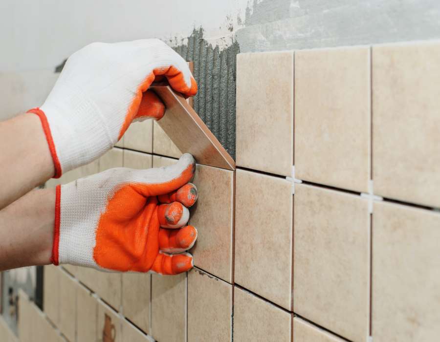 Worker sets  tiles on the wall in the kitchen. His hands are placing the tile on the adhesive.