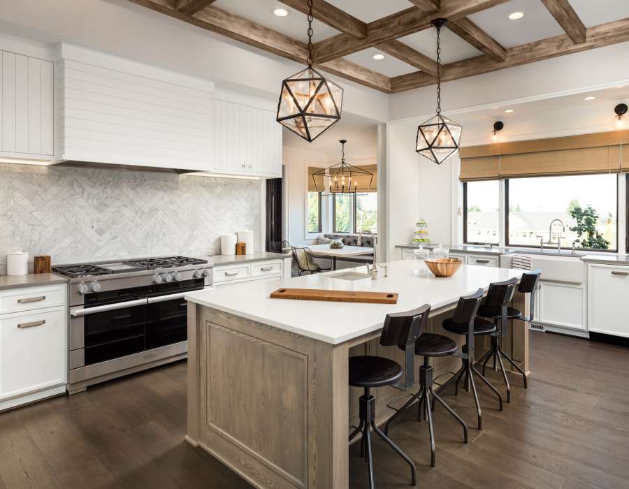 beautiful kitchen in new luxury home with island and pendant light fixtures Kitchen Interior with Island, Sink, Cabinets, and Hardwood Floors in New Luxury Home. Includes elegant pendant light fixtures and wood beam ceiling