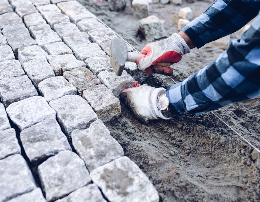 industrial worker installing pavement rocks, cobblestone blocks on road pavement